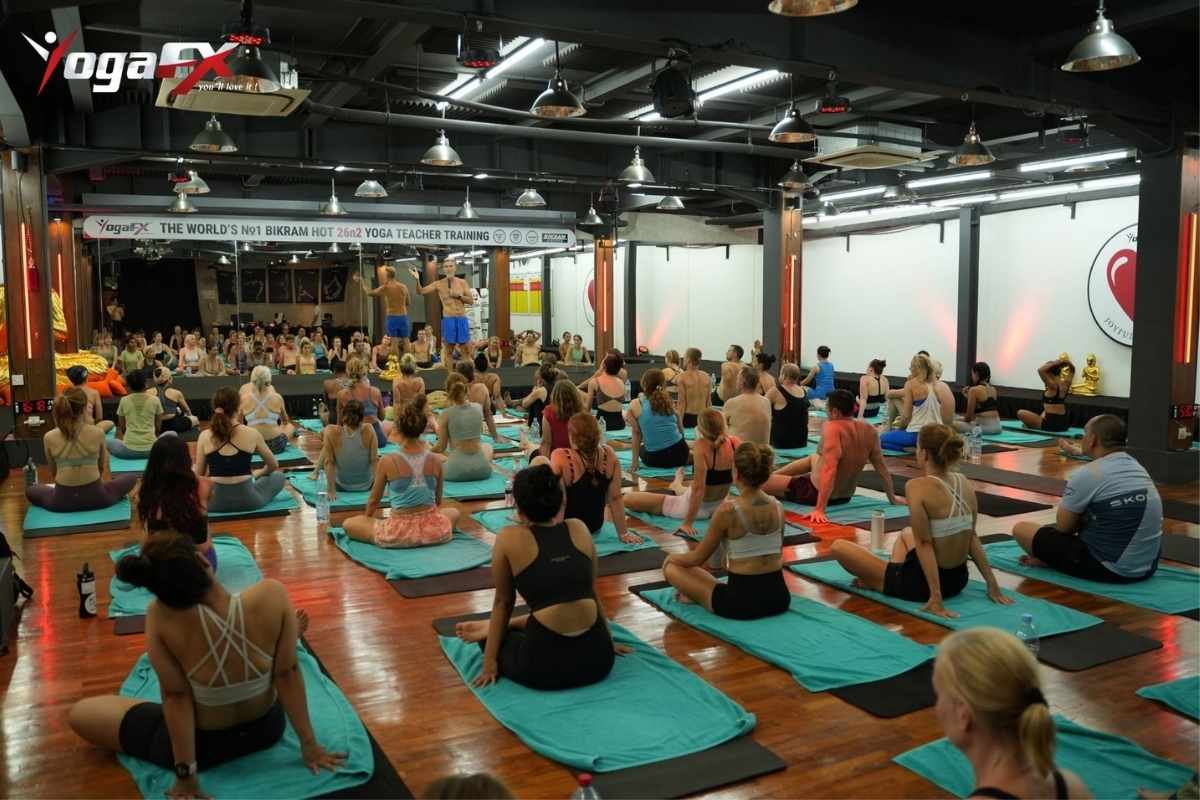 Hot yoga participant resting with a water bottle and sweat towel on a mat