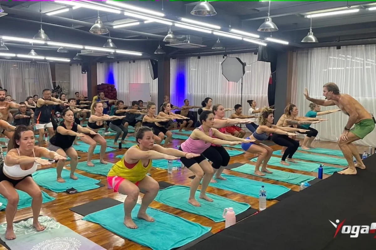Hot vinyasa vs Bikram: students in chair pose during a fixed-sequence Hot 26&2 class led from the front of the room