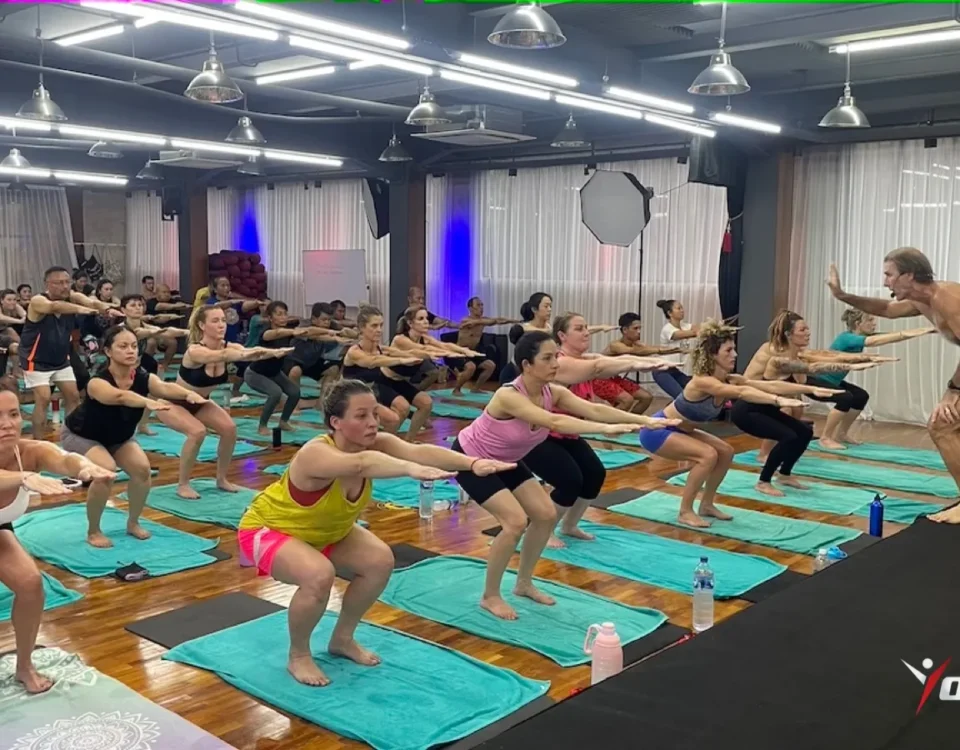 Hot vinyasa vs Bikram: students in chair pose during a fixed-sequence Hot 26&2 class led from the front of the room