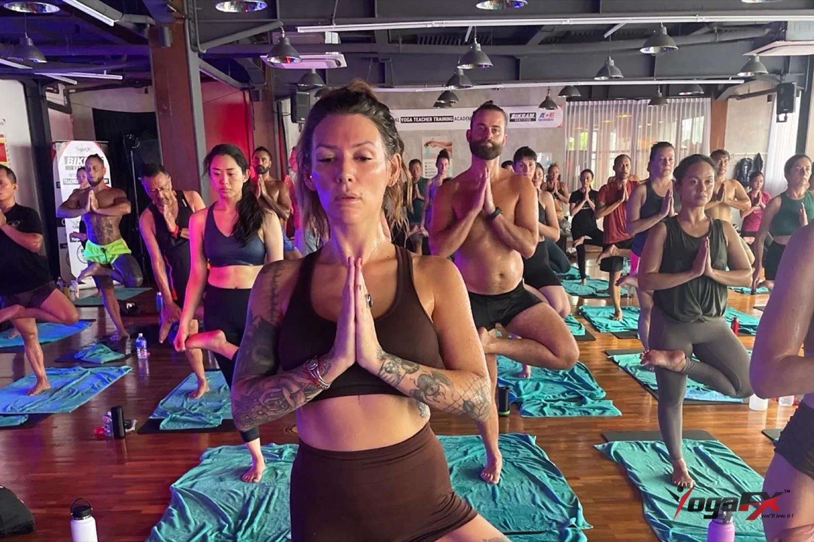 Hot vinyasa vs Bikram: students in tree pose with hands in prayer, showing the stillness of a fixed Hot 26&2 sequence