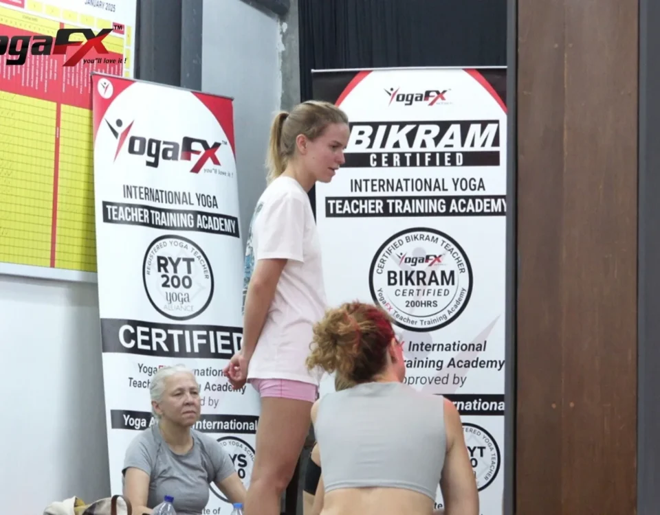Trainee at a YogaFX teacher training in front of RYT 200 and Bikram Hot 26&2 certified banners, the dual certification behind how much yoga teachers earn