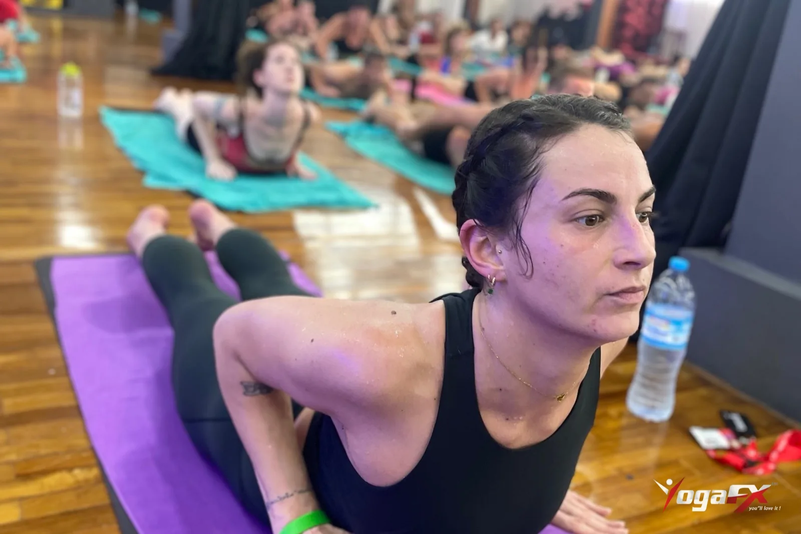 A student holding Cobra Pose on a purple mat with a water bottle beside her and the class lying behind