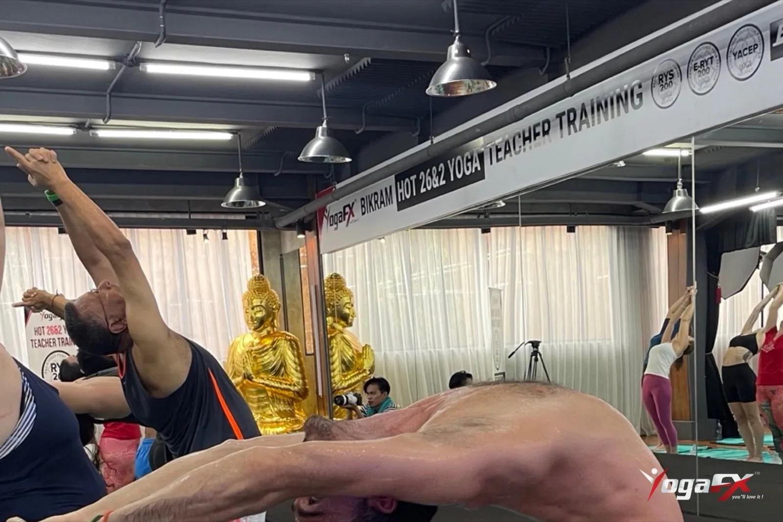 A man holding a deep standing backbend in a hot yoga class, showing the spinal mobility men can build