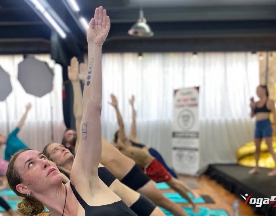 Yoga benefits for men and women alike: a full hot yoga class standing in a side-bend stretch on teal mats